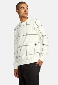 Jasno beżowy sweatshirt z czarnym wzorem w kratę, okrągłym dekoltem i długimi rękawami, wykonany z miękkiej tkaniny bawełnianej z domieszką, z prążkowanymi mankietami.