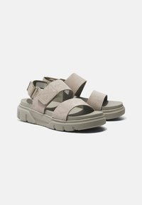 Beige semišové sandály s gumovou podrážkou, širokými pásky a nastavitelným páskem na patě. Plochý design, minimalistické akcenty a hladký povrch.