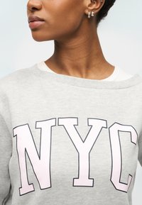 Γκρι φούτερ με μεγάλο ροζ τύπωμα "NYC". Διαθέτει λαιμόκοψη σκάφους και απαλή, υφή υφάσματος.
