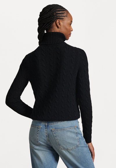 Svart kabelstickad polotröja med en figurnära stil. Har långa ärmar och ett strukturerat mönster. Bärs med ljusblå jeans.
