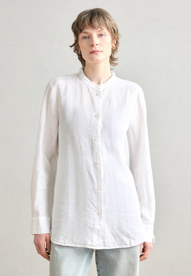 Witte langarmshirt van textuurstof, met een mandarin collar en een knoopsluiting aan de voorkant, gecombineerd met blauwe jeans.