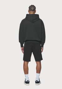 Musta huppari kenguru-taskulla, yhdistetty mustiin farkkushortseihin. Rentoa istuvuutta ja resorireunukset hihansuissa. Valkoiset lenkkarit ja nilkkasukat.