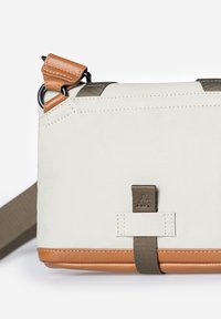 Crossbodytas gemaakt van crèmekleurige stof met cognackleurige leren accenten, voorzien van een bruine band en een geometrisch logodetail. Compacte rechthoekige vorm.