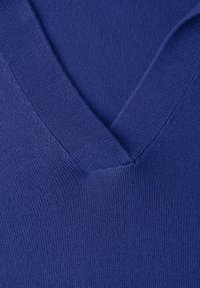 Gros plan sur un vêtement tricoté bleu présentant un col en V avec une texture côtelée détaillée et des coutures apparentes.