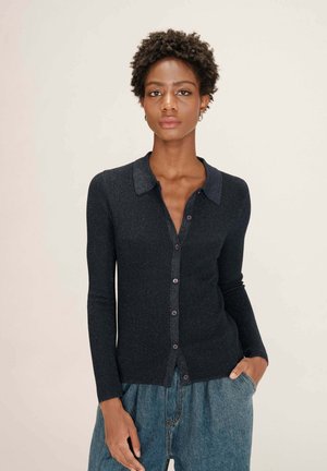 Cardigan marine avec un col, fermeture à boutons et texture côtelée. Manches longues avec un léger reflet, associé à un pantalon en denim ample.