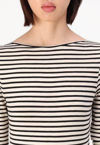 Svart- og hvitstripet topp med en myk tekstur, vid båtbhals og lange ermer, med jevne horisontale striper.