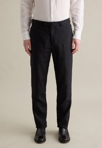 Pantalones de lino negros con corte recto y cierre de botón, combinados con una camisa blanca de botones. Textura suave y ajuste a medida.