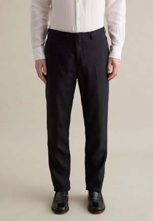 Pantalones de lino negros con corte recto y cierre de botón, combinados con una camisa blanca de botones. Textura suave y ajuste a medida.