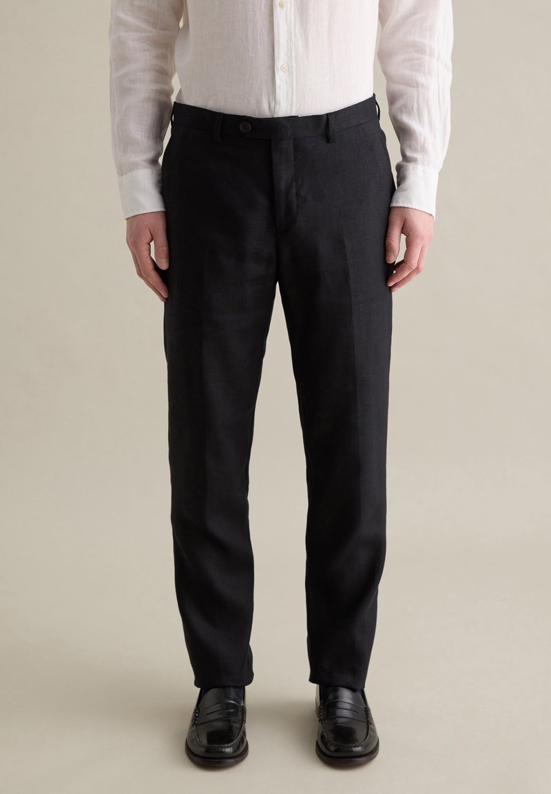 Pantalones de lino negros con corte recto y cierre de botón, combinados con una camisa blanca de botones. Textura suave y ajuste a medida.