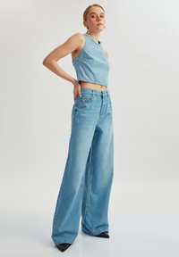 Top de tirantes corto de mezclilla azul claro combinado con jeans holgados de mezclilla azul claro. Cintura alta, ligeros desgastes en los bordes y zapatos de punta negra.