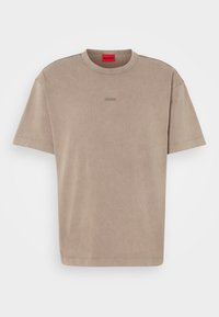 T-shirt en coton beige avec col rond, manches courtes et un logo subtil de la même couleur sur la poitrine. Design texturé et décontracté.