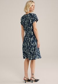 Robe bleu marine à manches courtes, présentant un motif texturé en vert clair et blanc. Silhouette en A avec un ourlet au niveau du genou.