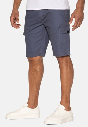 Dunkelblaue Cargo-Shorts aus atmungsaktivem Material, mit seitlichen Taschen und Gürtelschlaufen. Kombiniert mit weißen Sneakers.