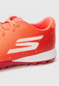 Adidași sport portocalii strălucitori cu un material texturat, șireturi plate și brand alb. Talpa este gri, dotată cu tălpi scurte pentru aderență.