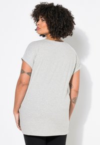 Camiseta de algodón gris claro con mangas enrolladas, de corte holgado y dobladillo redondeado, que presenta una textura sutil y un diseño sin adornos.