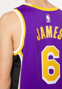 Canotta da basket viola con dettagli gialli, con il nome "JAMES" e il numero "6" sul retro. Realizzata in tessuto a rete traspirante.