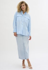 Light blue button-up shirt with two front pockets, paired with a knee-length light denim skirt. The fabric appears smooth and untextured.