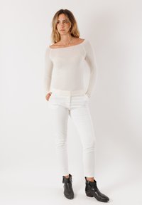 Camicia bianca a maniche lunghe con scollatura aperta, abbinata a pantaloni bianchi aderenti e stivaletti neri alla caviglia. Tessuto liscio e design avvolgente.