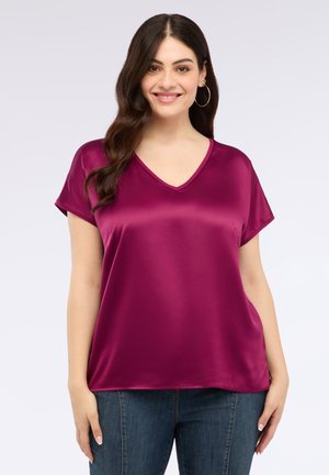 Magenta satijnen top met een V-hals, korte mouwen en een relaxte pasvorm. Glad textuur en lichte glans, gecombineerd met donkere denim jeans.
