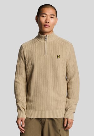 Beige ribbed sweater with a high collar and quarter-zip, featuring a small yellow logo on the chest. Soft texture and fitted design.