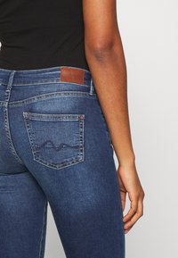 Blå denimjeans med en läderlapp vid bakliv, med en dekorativ sömnadsdesign på bakfickan. Slimmad passform.