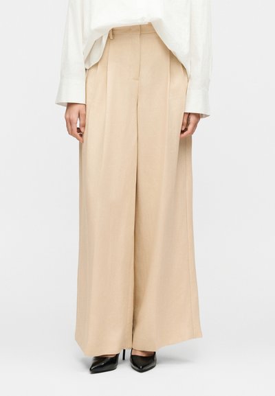 Beige wide-leg trousers paired with black pointed high heels and a white long-sleeve shirt against a plain background.