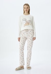Cream long-sleeve top with coffee and croissant print, paired with light pink pajama pants featuring croissant patterns. Fluffy beige slippers.