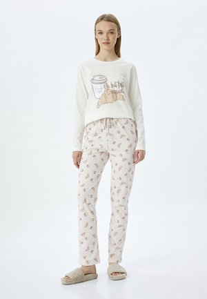 Crème kleurige blouse met lange mouwen, bedrukt met koffie en croissant, gecombineerd met lichtroze pyamabroek met croissantpatronen. Fluffy beige slippers.