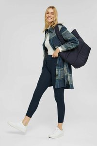 Cappotto a quadri blu e verde, maglione bianco a coste, leggings blu marino e sneakers bianche. La modella porta una borsa a tracolla nera e imbottita.
