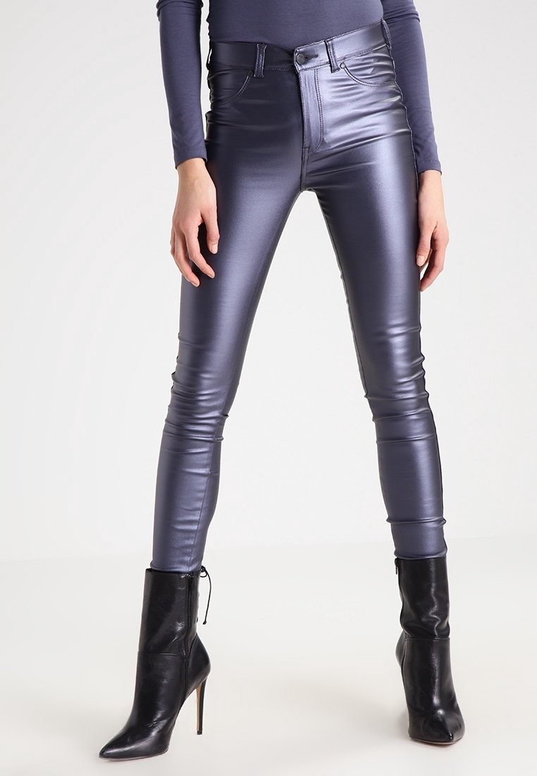 Pantalon en cuir gris foncé brillant, coupe slim, porté avec des bottines noires à talons hauts et un top gris à manches longues.