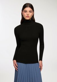 Czarny, prążkowany sweter z golfem i długimi rękawami, z dopasowanym krojem. W zestawie z plisowaną niebieską spódnicą.