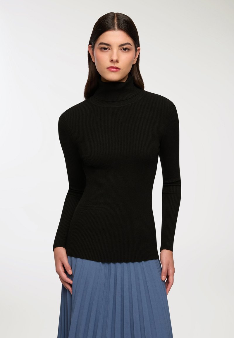 Czarny, prążkowany sweter z golfem i długimi rękawami, z dopasowanym krojem. W zestawie z plisowaną niebieską spódnicą.