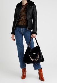 Czarna torebka z futra ekologicznego z akcentem w postaci łańcuszka, z górną klapą. Stylizowana z skórzaną kurtką, wzorzystą bluzką, niebieskimi dżinsami i brązowymi botkami za kostkę.