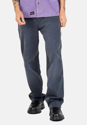 Dunkelgraue Jeans mit einer lässigen Passform, aus Denim gefertigt, kombiniert mit schwarzen Schuhen mit grober Sohle. Die Jeans haben dezente Stickdetails.