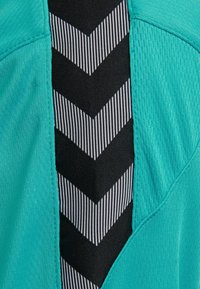 Türkiser Stoff mit strukturiertem Finish, der in der Mitte ein schwarzes Paneel mit vertikalen Streifen und Chevron-Muster aufweist.