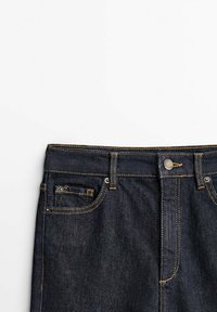 Granatowe dżinsy o klasycznym kroju, widoczne szwy, zapięcie na guzik i kieszenie z przodu. Gładka textura i regularny krój.