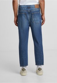 Siniset denim-housut suoran lahkeen istuvuudella, viisi taskua ja ruskea nahkainen brändilogo takavyötäröllä. Rakennepintainen kangas.