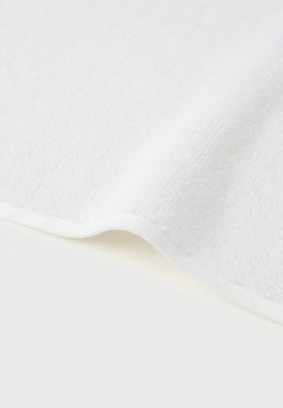 Tela blanca suave con una superficie ligeramente texturizada y un borde curvado sobre un fondo blanco