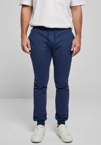 Tamsiai mėlyni sportiniai treningai su elastine juosmens juosta ir raišteliu, su ribotomis rankogaliais ir lygiu paviršiumi. Derinami su baltais sportbačiais.