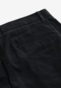 Tissu noir en gros plan montrant la poche arrière et les passants de ceinture d'un pantalon.