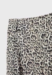 Pantalon taille haute en tissu imprimé léopard noir et blanc avec deux boutons blancs à la taille.