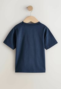 Tumesinist lühikeste varrukatega t-särki, mis on valmistatud siledast puuvillakangast, millel on ümara kaelusega ja mugava istuvusega, eksponeeritud puidust riidepuul.