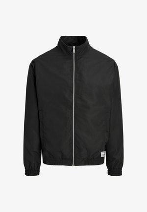 Must kerge jope eesrihmaga, kõrge krae, elastsete varrukaotste ja äärega ning väike valge ristkülikukujuline silt ääre lähedal.