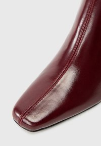 Botină din piele burgundy, cu vârf ascuțit, textură netedă și cusături contrastante pe lateral.