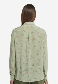 Grøn blomstret bluse med lange ærmer, bl�ødt stof, lyse rosa og hvide blomstermønstre samt en klassisk krave. Har knaplukning ved ærmerne.