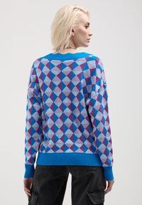 Maglione lavorato a maglia colorato con un motivo geometrico di triangoli in azzurro chiaro, viola e blu scuro. Polsini e orlo a coste.