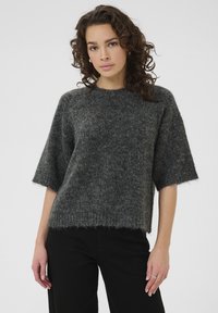 Grijze, gestructureerde trui met korte mouwen en een losse pasvorm, voorzien van een ronde halslijn en een franjeszoom, gecombineerd met zwarte broek.