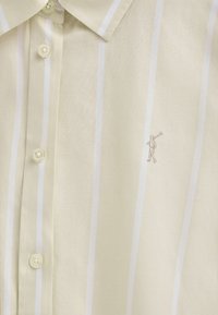 Camicia button-up gialla chiara con righe bianche, dotata di colletto classico e logo ricamato di una figura che tiene una mazza da golf.