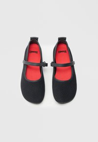 Czarne buty typu Mary Jane z siateczki, z czerwonym wnętrzem, wyposażone w regulowany pasek i zaokrąglony nosek, zapewniające przewiewność i komfort.