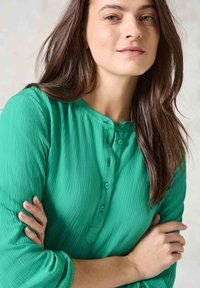 Grön, texturerad blus med knappst�ängning, rundad halsringning och trekvartsärmar. Har veckad tyg för extra detalj.